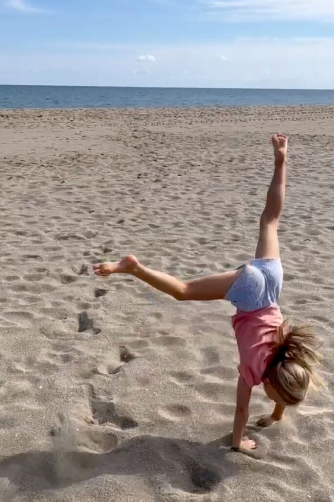 Kind macht ein Rad am Strand im Sand, im Hintergrund Meer und blauer Himmel
