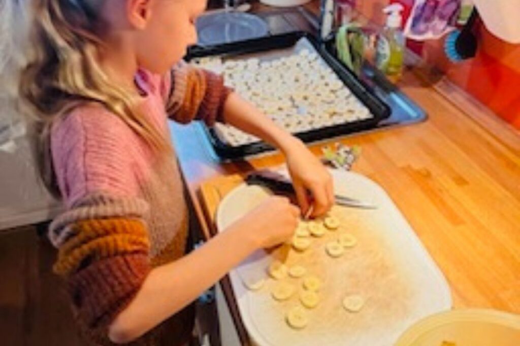 Kind schneidet Banane in der Küche und lernt durch eigenen Tun im Alltag