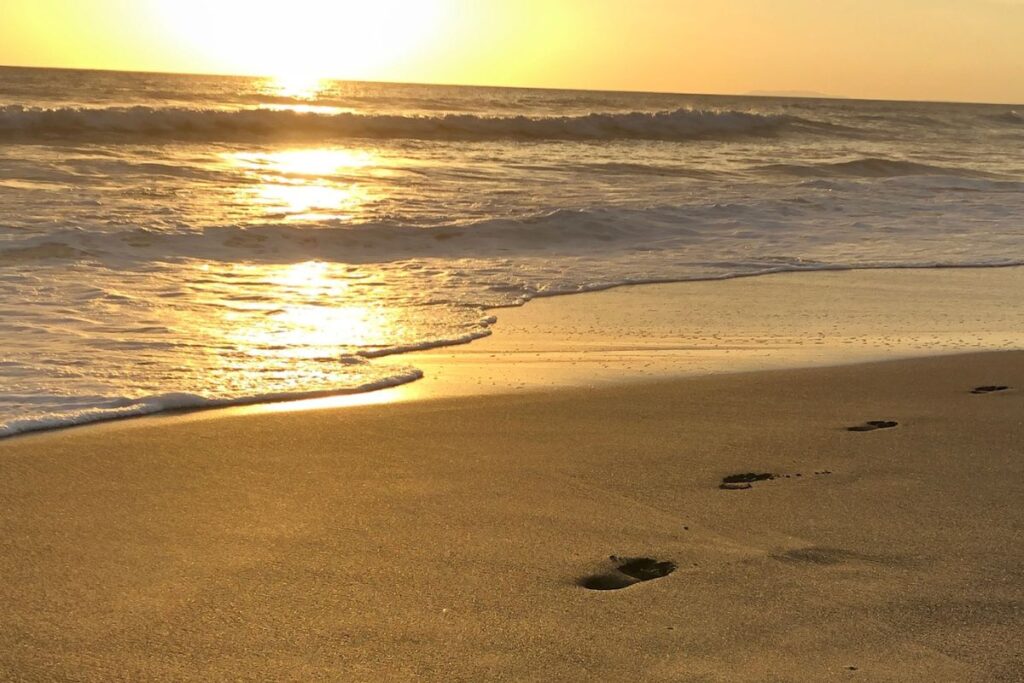 Sonnenuntergang am Meer mit Wellen und Fußspuren im Sand - ruhiger Moment am Strand