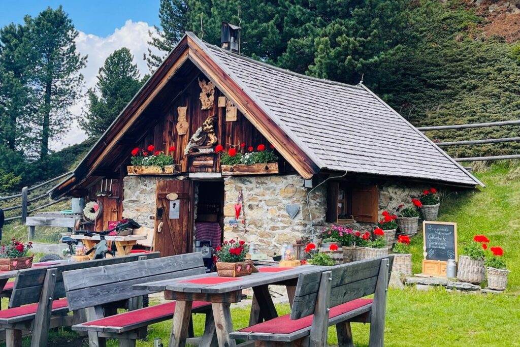 Rustikale Kalbenalm im Pitztal mit gemütlicher Sonnenterrasse, Blumenschmuck und Waldkulisse in den Tiroler Alpen.