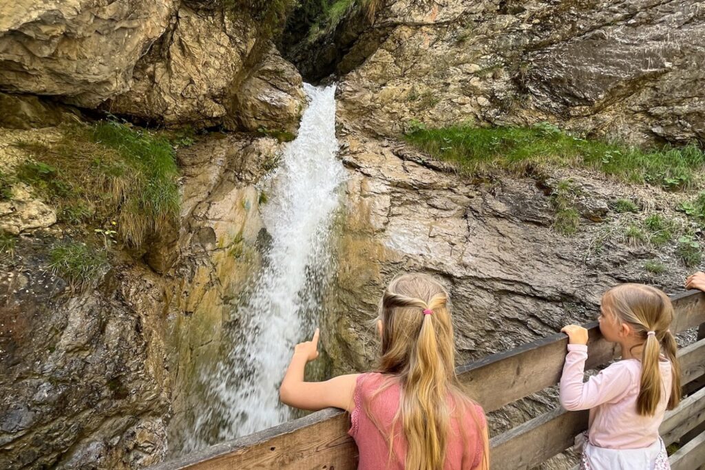 Zwei Kinder beobachten einen Wasserfall in der Rosengartenschlucht bei Imst in Tirol und entdecken die beeindruckenden Kraft des Wassers entlang des Schluchtwegs.