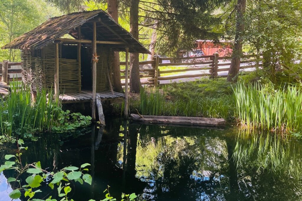 Nachgebaute Pfahlbauhütte mit Einbaumboot am Teich im Freilichtmuseum des Ötzi-Dorfs Umhausen.